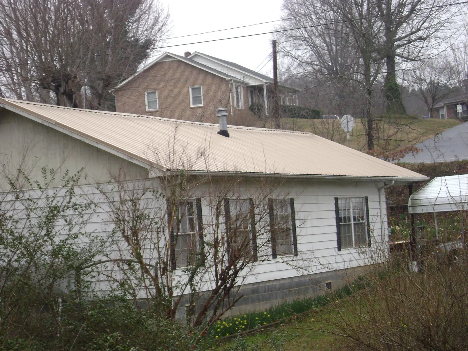 Tan metal roof on a white sided house set into a hillside — Commercial Roofing by Roofing Brothers in Humboldt